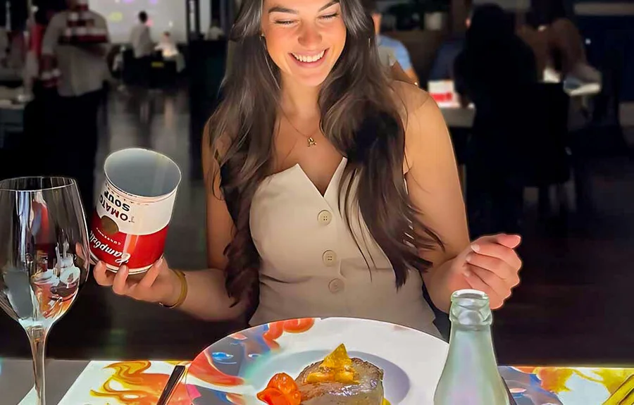 A guest holding the Campbell's Tomato Soup can from the Warhol course at her projection-lit table