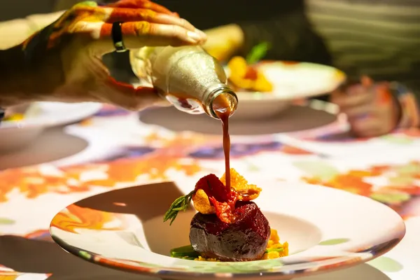 A course being finished at the table with a glittering sauce pour